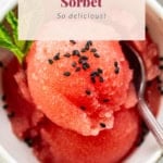 A bowl of watermelon sorbet topped with black sesame seeds, garnished with mint leaves, with text overlay reading "watermelon sorbet, so delicious!.