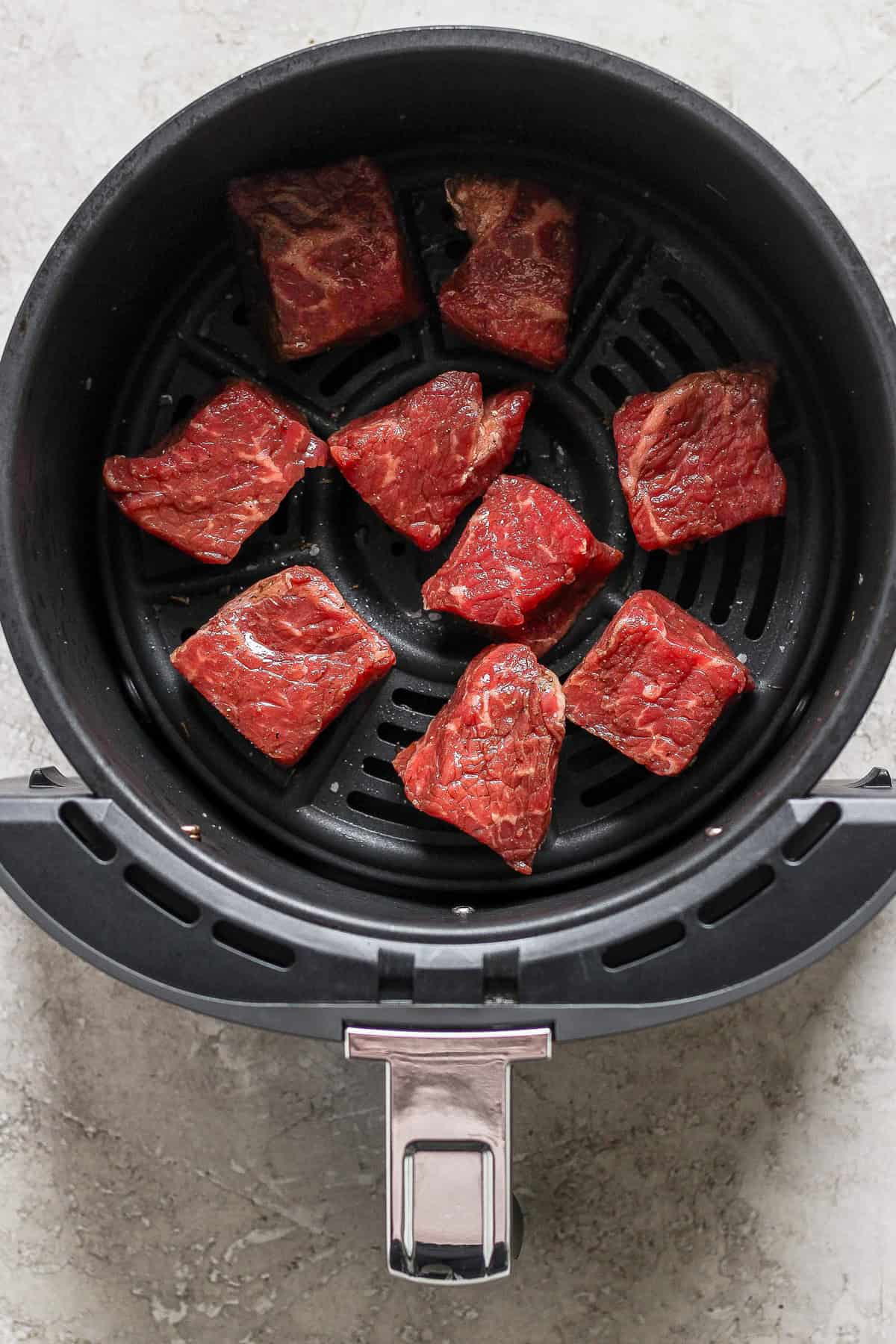 Raw beef pieces arranged in an air fryer basket, ready for cooking.