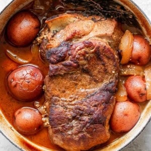 A cooked pot roast with potatoes and onions in a white enameled cast iron pot.