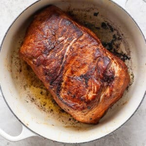 A cooked, browned piece of meat in a white pot, showing seared and crispy edges.