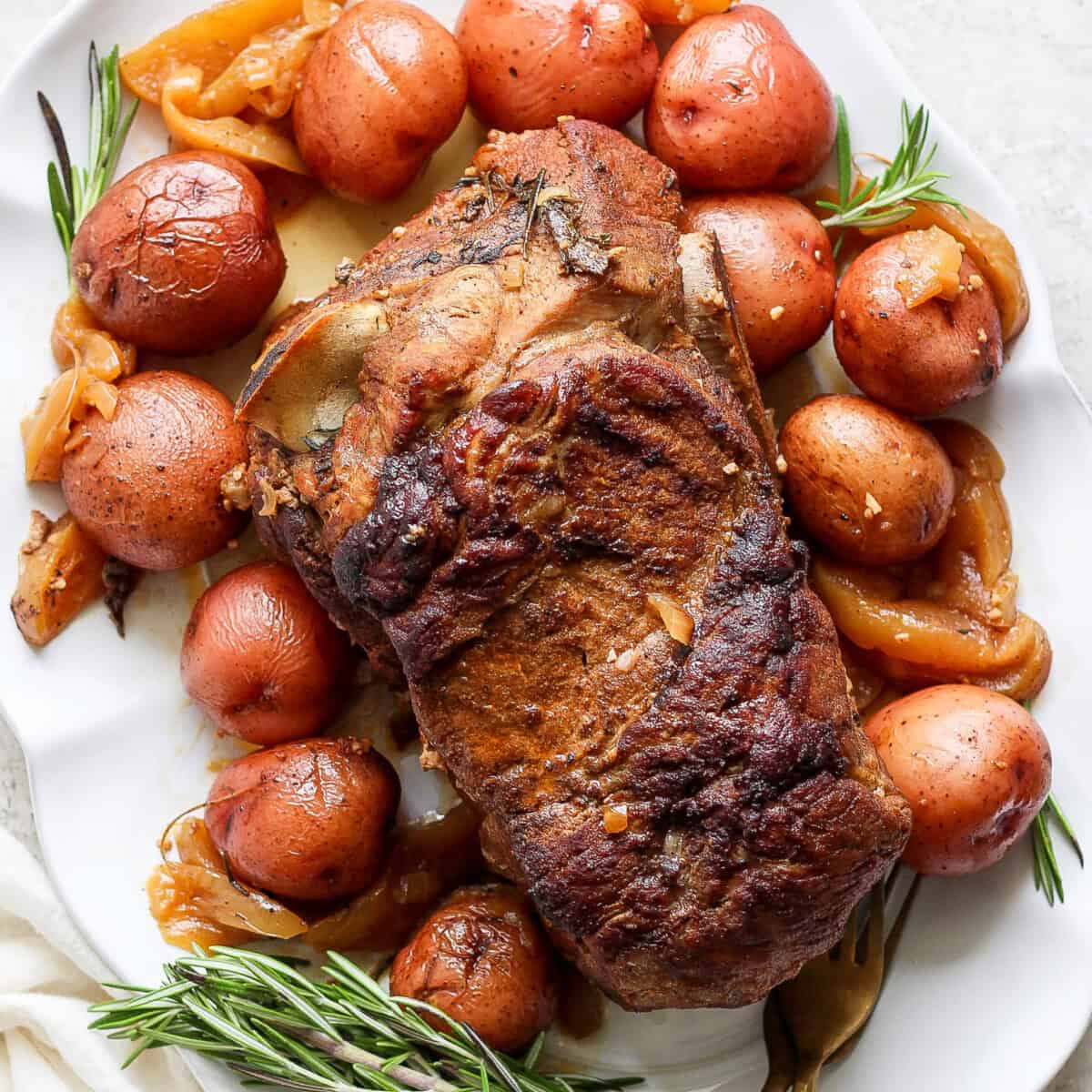 An oven-roasted pork roast surrounded by reddish  potatoes and garnished with rosemary connected  a achromatic  platter.