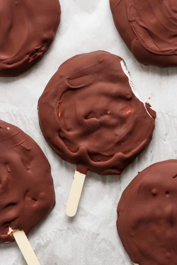 Chocolate-covered ice cream bars on sticks, viewed from above, with one bar having a bite taken out of it.