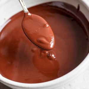 A spoon is held above a bowl of melted chocolate.