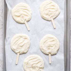 Four raw popsicle-shaped dough pieces on parchment paper in a gray baking tray.