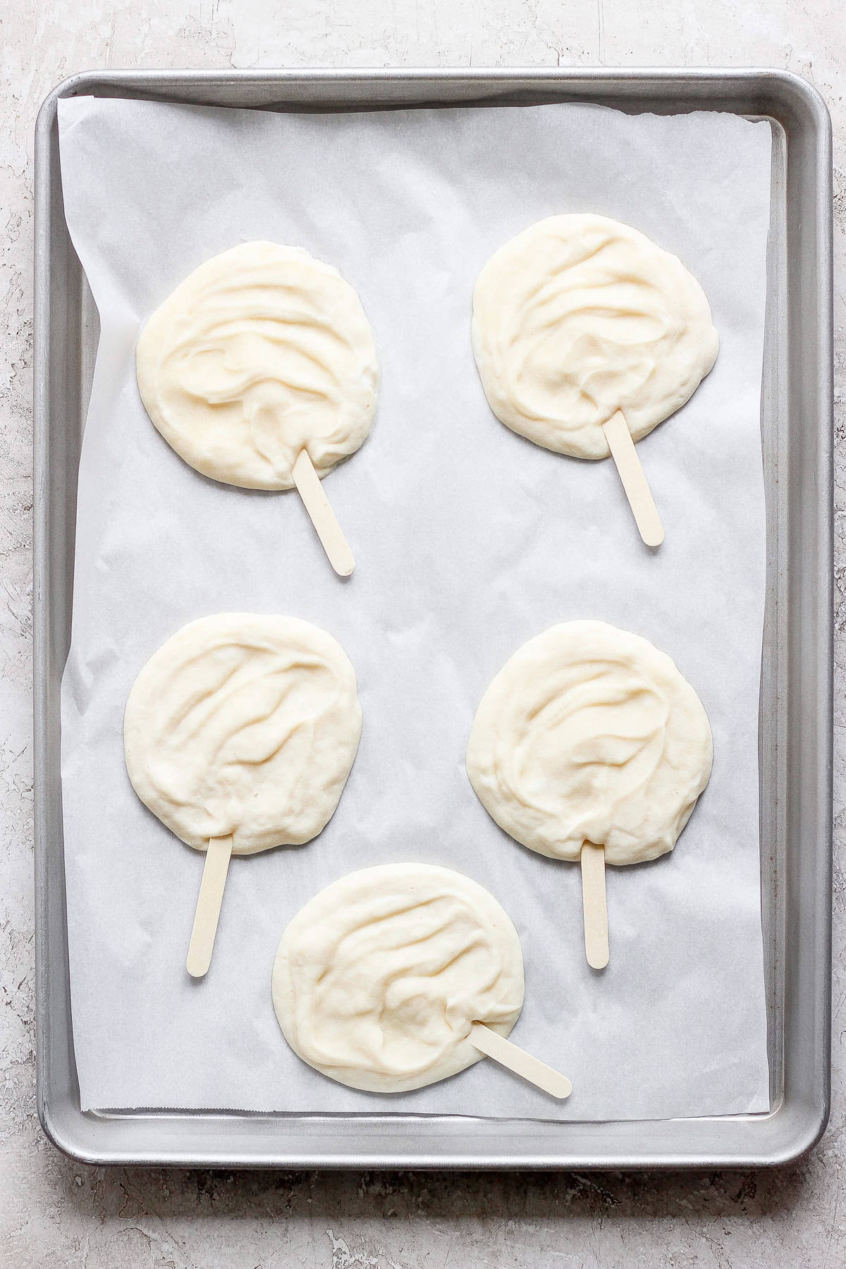 Four raw popsicle-shaped dough pieces on parchment paper in a gray baking tray.