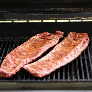 Two racks of seasoned ribs cooking on an open grill.