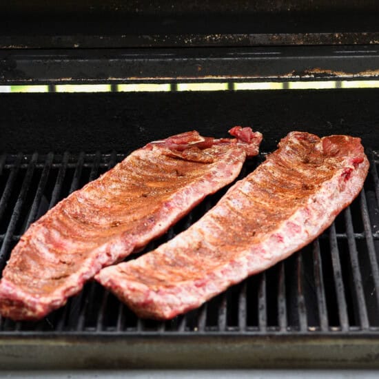 Two racks of seasoned ribs cooking on an open grill.