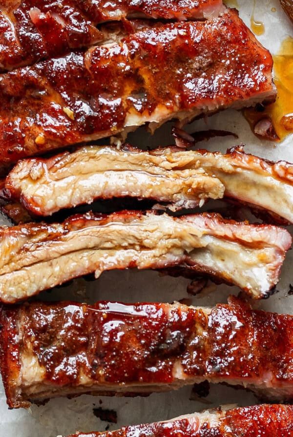 Close-up view of several pieces of glazed, barbecued ribs on parchment paper, with a brush coated in sauce to the side.