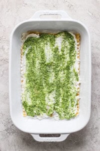 A white baking dish containing an uncooked layered green and white lasagna against a textured light gray surface.