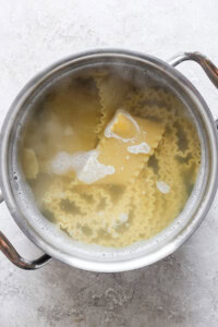 A pot filled with boiling water and lasagna noodles on a stovetop.