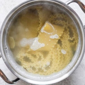 A pot filled with boiling water and lasagna noodles on a stovetop.