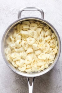 A pot filled with cooked cheese tortellini sitting on a light-colored surface.