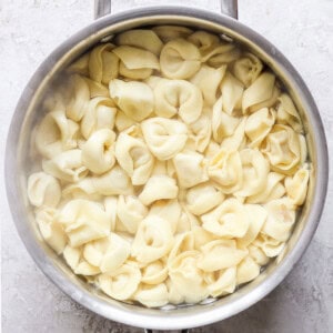 A pot filled with cooked cheese tortellini sitting on a light-colored surface.