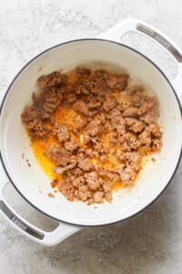 Ground beef browning in a white Dutch oven on a gray surface.