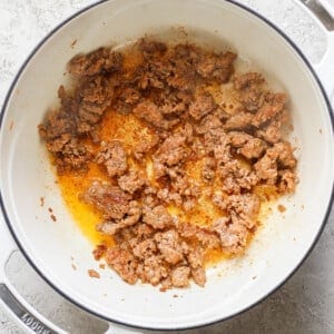 Ground beef browning in a white Dutch oven on a gray surface.