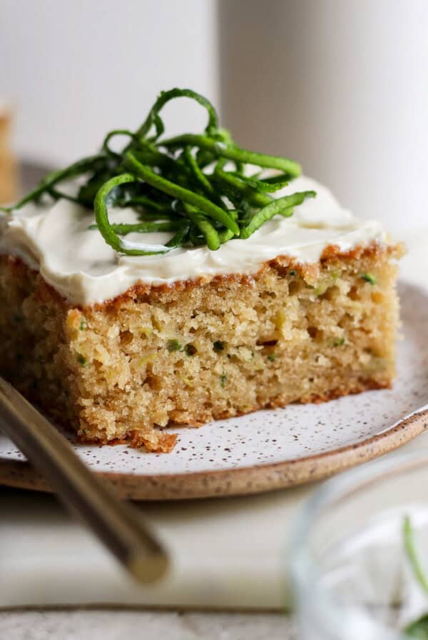 A slice of cake with white frosting and green garnish on a speckled plate, accompanied by a fork.