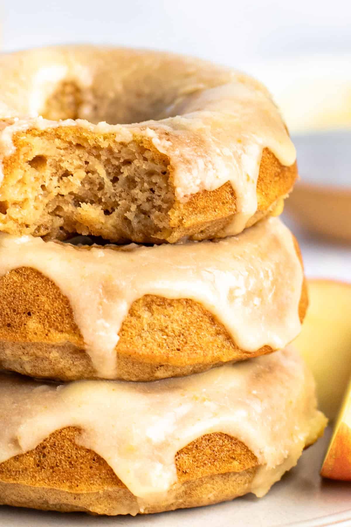 A stack of three glazed donuts with a bite taken out of the top one, showing their soft interiors.