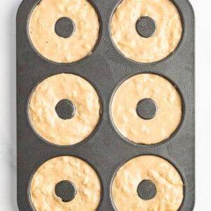 A six-cavity donut baking pan filled with unbaked donut batter, ready to be placed in the oven.