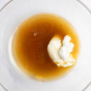 A glass bowl containing a mixture of liquid honey and a dollop of yogurt.