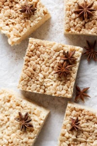 Square rice crispy treats with a dusting of spices and garnished with star anise, arranged on a parchment paper surface.