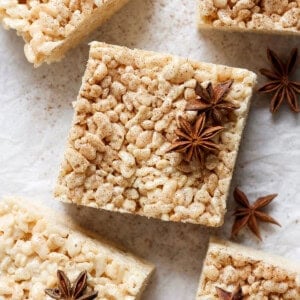 Square rice crispy treats with a dusting of spices and garnished with star anise, arranged on a parchment paper surface.