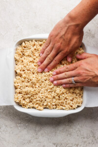 Hands pressing down on a tray of rice crispy treats to flatten and shape them.