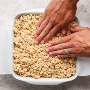 Hands pressing down on a tray of rice crispy treats to flatten and shape them.