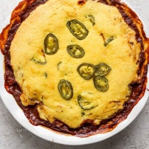 A baked dish in a round white pan, topped with cornbread and sliced jalapenos, with some edges browned and crispy.