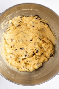 A metal mixing bowl containing a dough mixture with visible chocolate chips and white chunks.