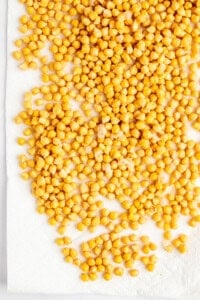 A large number of yellow chickpeas spread out on a white paper towel.