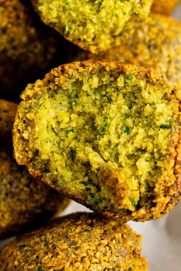 Close-up of a halved falafel, revealing its green, crispy interior. Other whole falafel pieces arrange in the background on parchment paper.