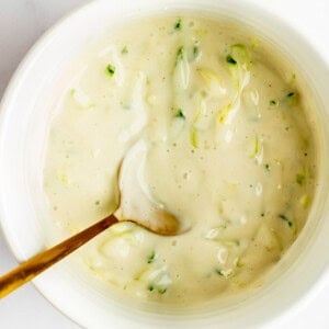 A bowl of creamy dressing with chopped green herbs and a spoon inside.