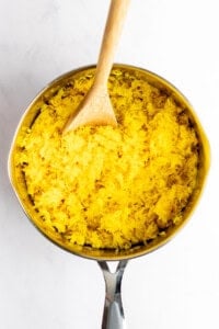 A saucepan filled with yellow rice and a wooden spoon resting inside.
