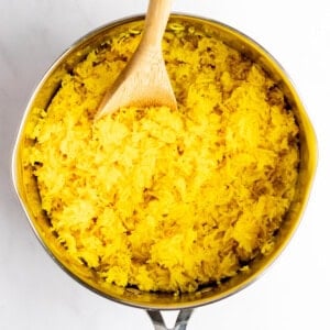 A saucepan filled with yellow rice and a wooden spoon resting inside.