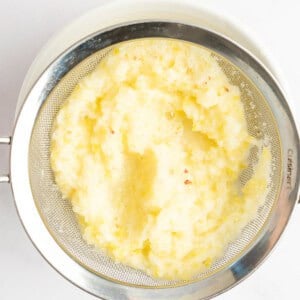 A metal sieve containing mashed potatoes over a white bowl.