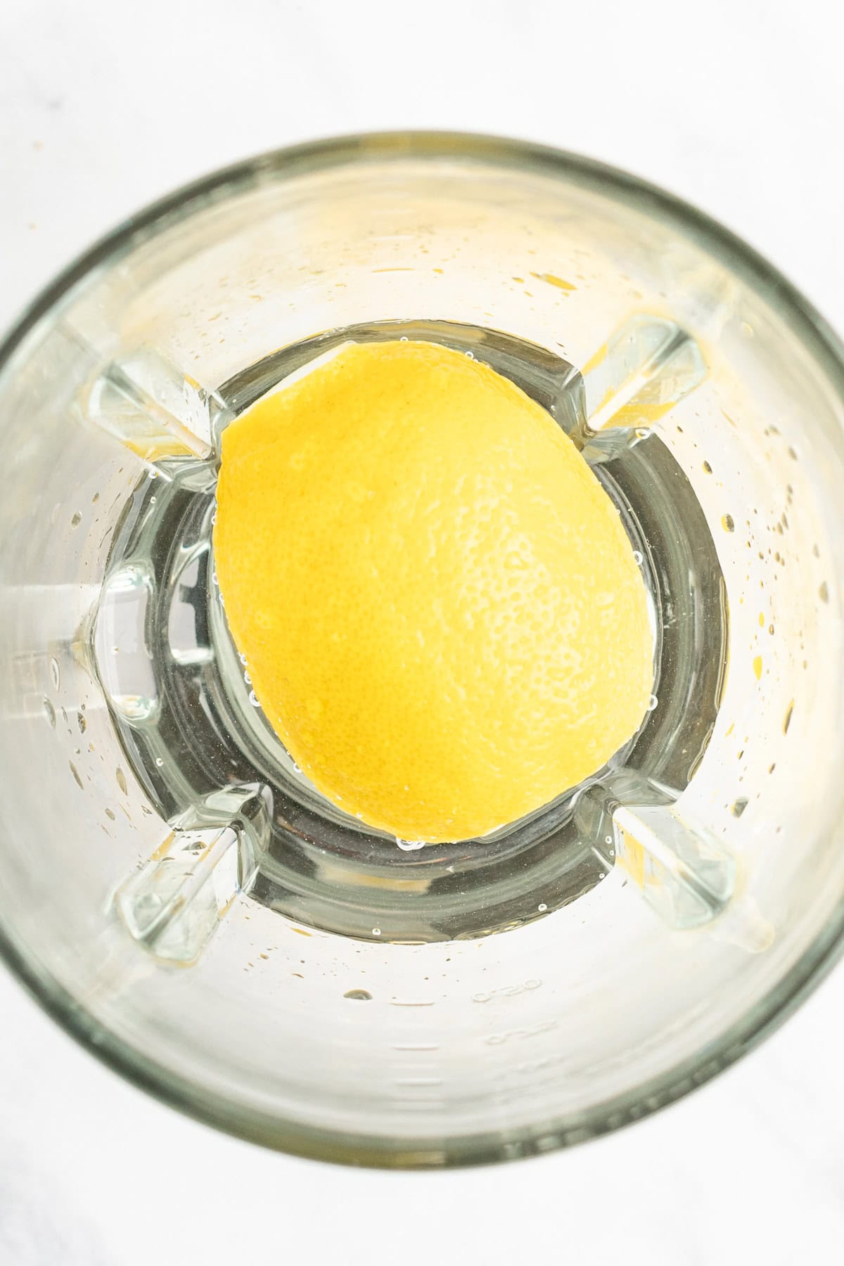 A halved lemon sits in a blender jar, viewed from above.