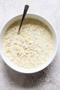 A bowl of oat mixture with chia seeds and grated lemon zest, reminiscent of creamsicle overnight oats, stirred with a spoon.