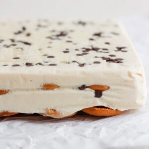 Close-up of a layered peanut butter banana ice box cake with a creamy white filling, chocolate chips on top, and a base of cookies, set on crinkled parchment paper.