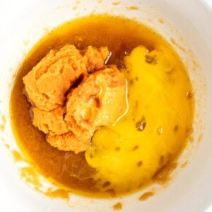 A mixing bowl contains mashed sweet potatoes, yolk-like liquid, and brown syrupy substance being prepared for a recipe.