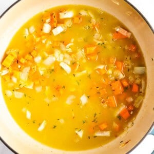 A pot of vegetable soup with chopped onions, carrots, and broth, simmering on the stovetop.