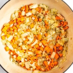 A pot containing sautéed diced onions and carrots.