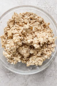 A glass bowl containing a mixture of oats and flour sits on a grey countertop.