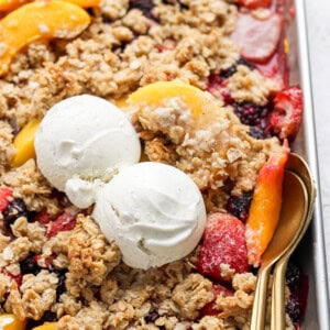 A dessert tray with fruit crisp topped with two scoops of vanilla ice cream and a spoon on the right side.