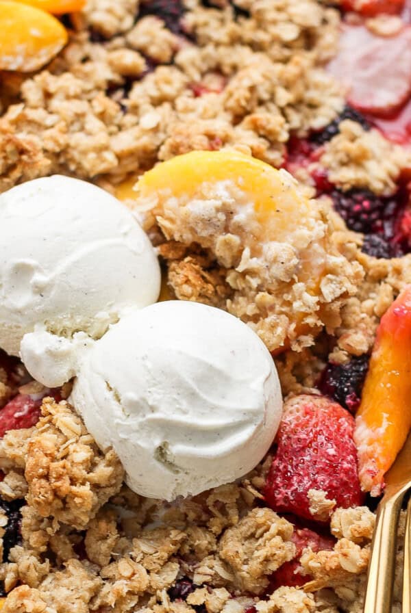 A dessert tray with fruit crisp topped with two scoops of vanilla ice cream and a spoon on the right side.