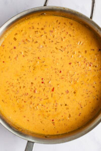 A metal pan filled with a thick, orange-colored soup or sauce that contains small pieces of diced vegetables.