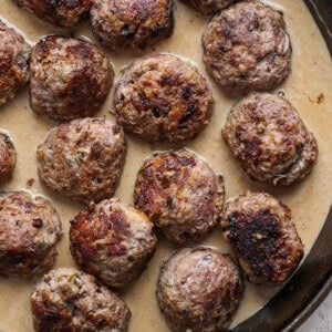 A skillet containing several browned meatballs in a creamy gravy.