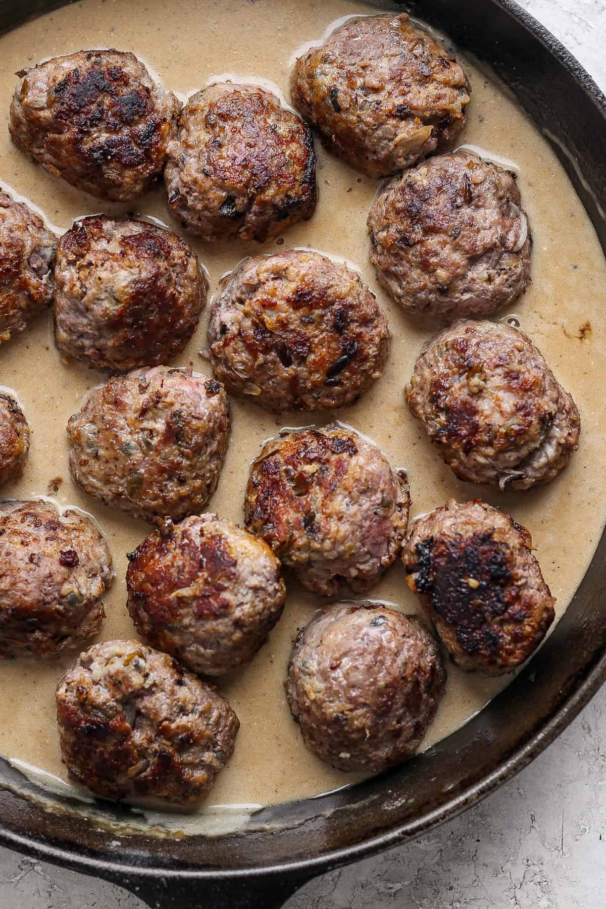 A skillet containing several browned meatballs in a creamy gravy.