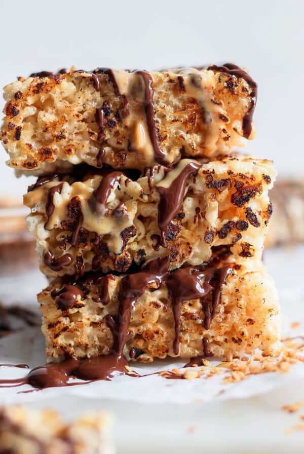 Stack of three toasted rice Krispie treats drizzled with chocolate and peanut butter on a white surface.
