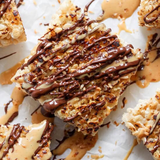 Close-up of toasted rice Krispie treats dessert bars topped with caramel and chocolate drizzle on a parchment paper background.