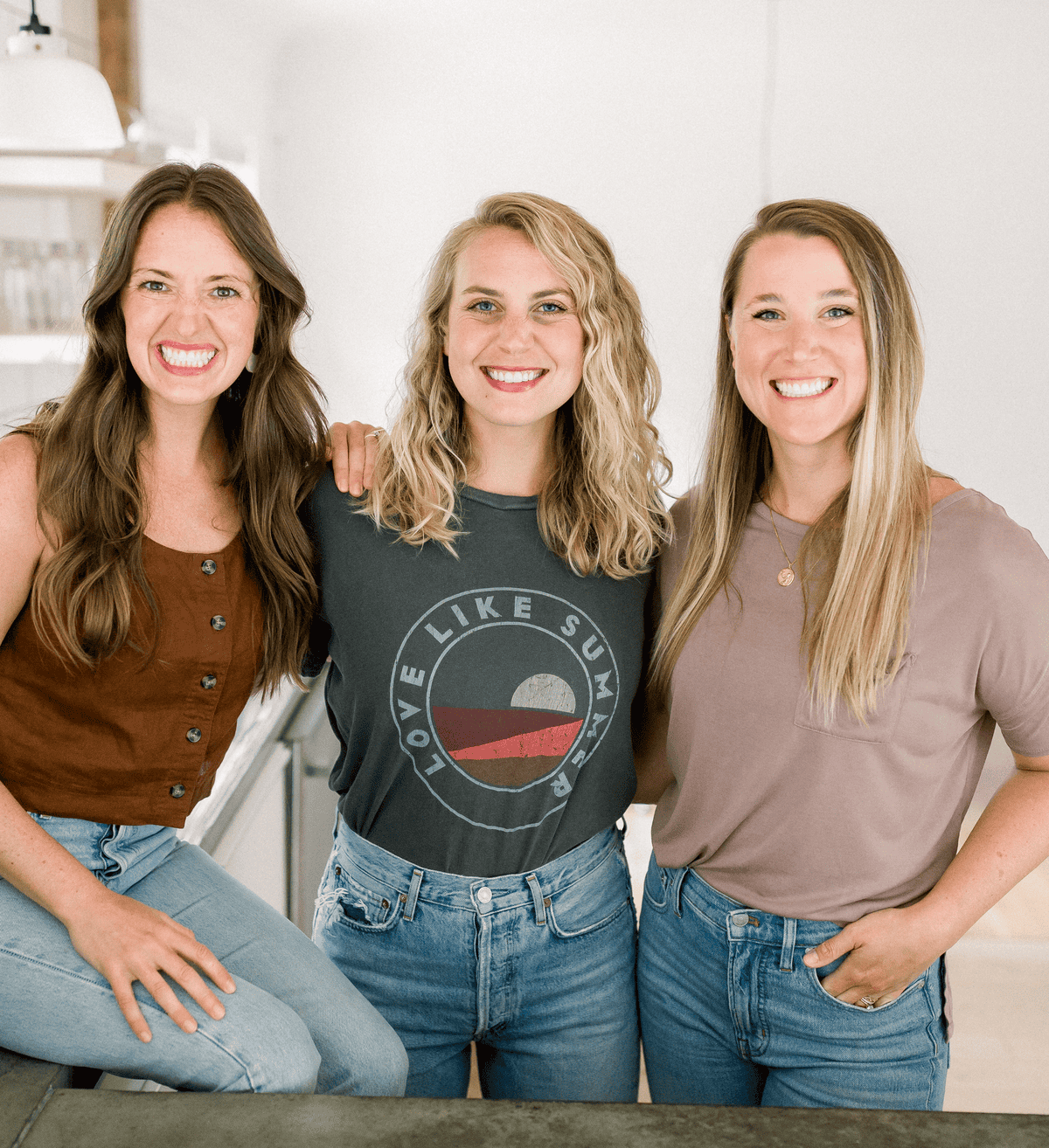 Three women, fit and radiant, stand closely together indoors, smiling at the camera. Each is dressed in casual wear, possibly sharing their latest foodie finds.